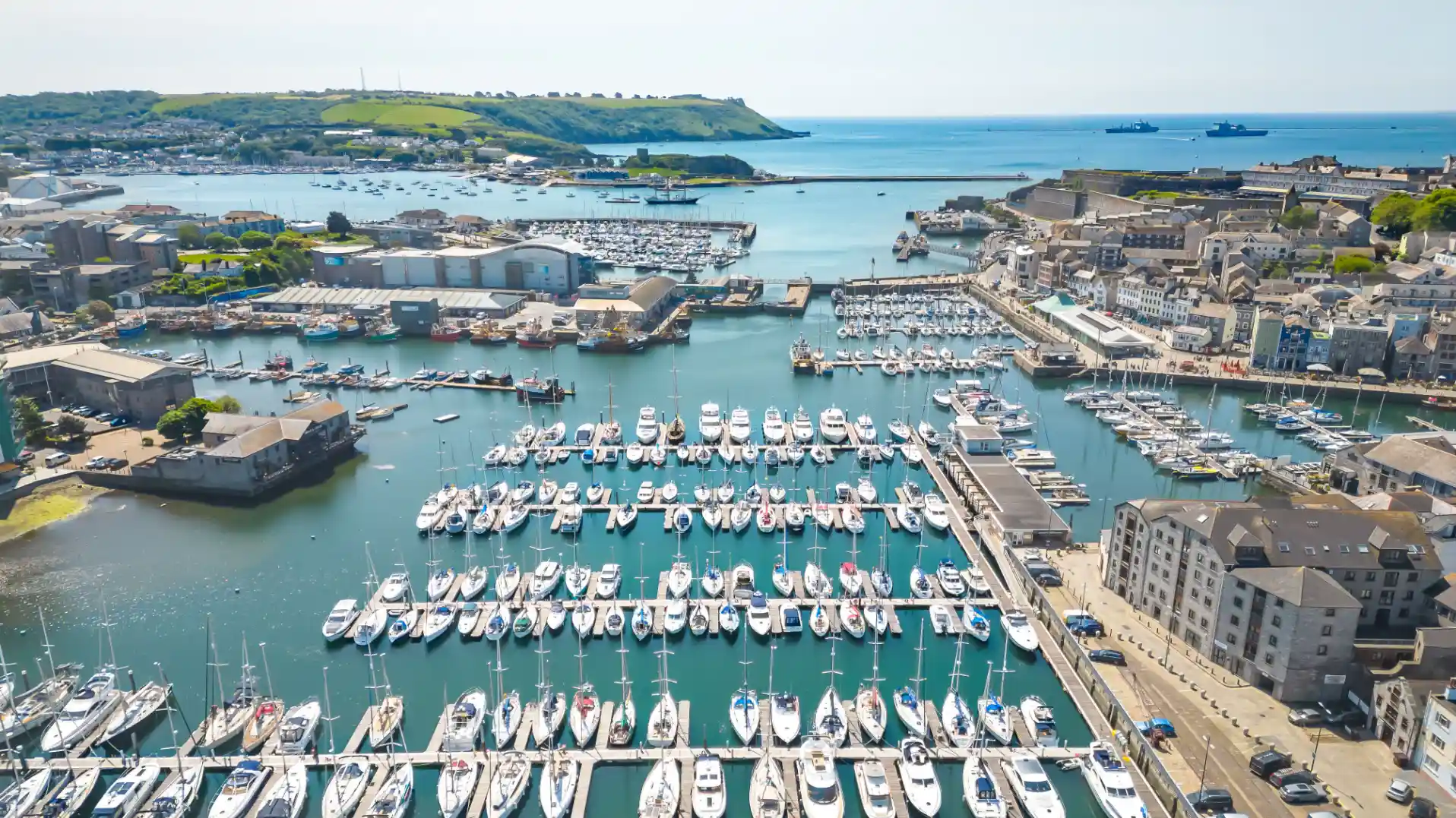 Aerial view of Sutton Harbour and the Barbican in Plymouth, with rows of yachts, the historic waterfront, and Plymouth Sound in the background.