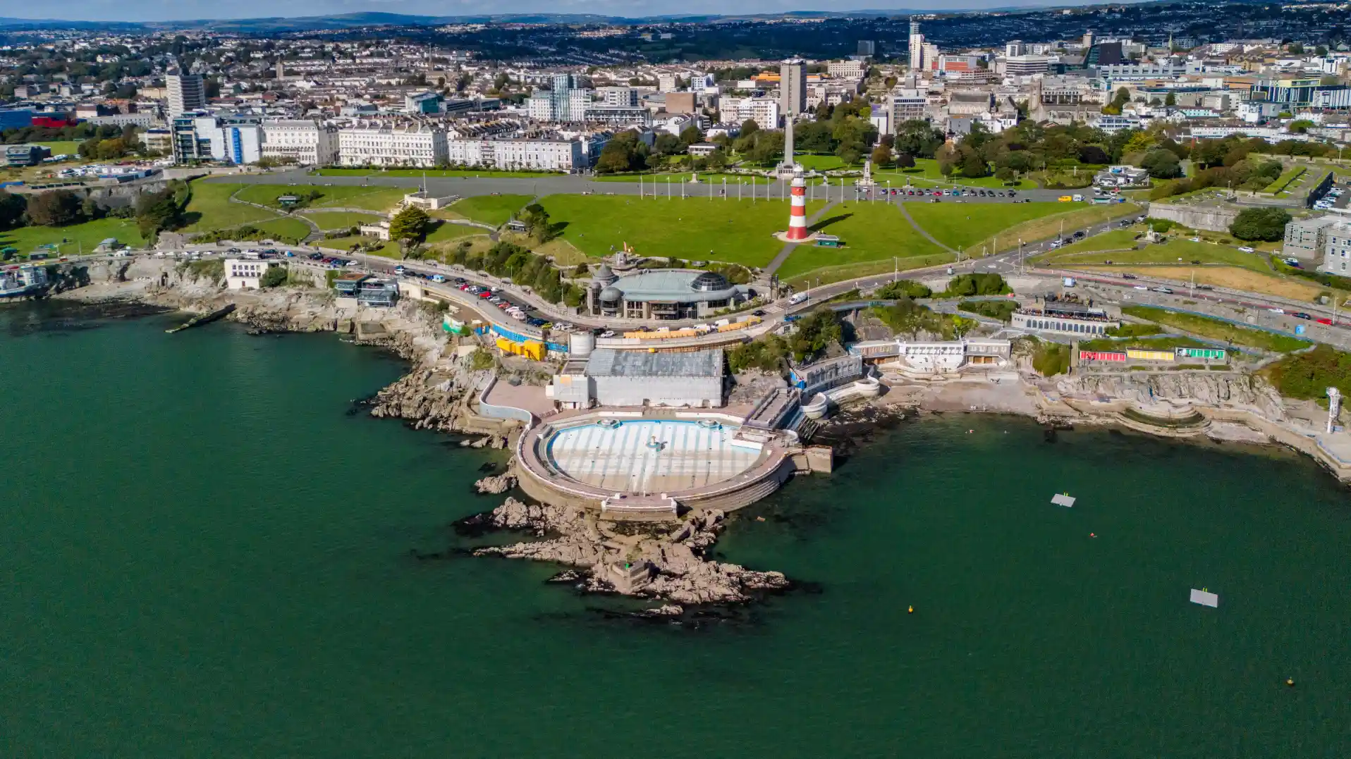 Aerial view of Plymouth Hoe showing Tinside Lido, Smeaton’s Tower, and the city skyline in the background.