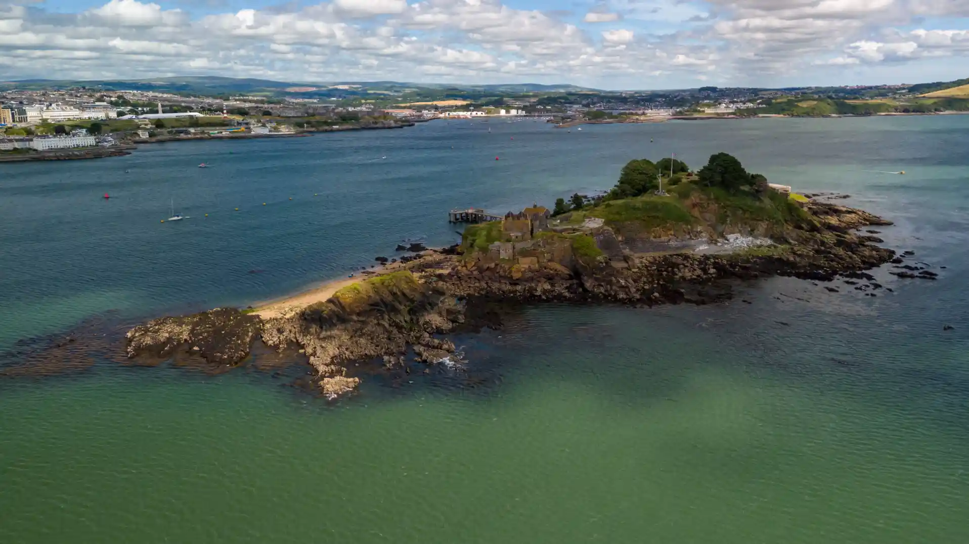 Aerial view of Drake’s Island in Plymouth Sound, showing its rocky coastline, historic buildings, and surrounding blue-green sea.