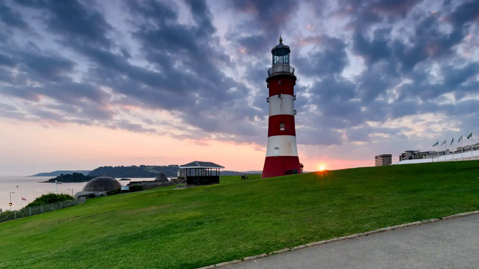 Smeaton’s Tower lighthouse on Plymouth Hoe at sunset, with green lawns in the foreground and the sea in the background.